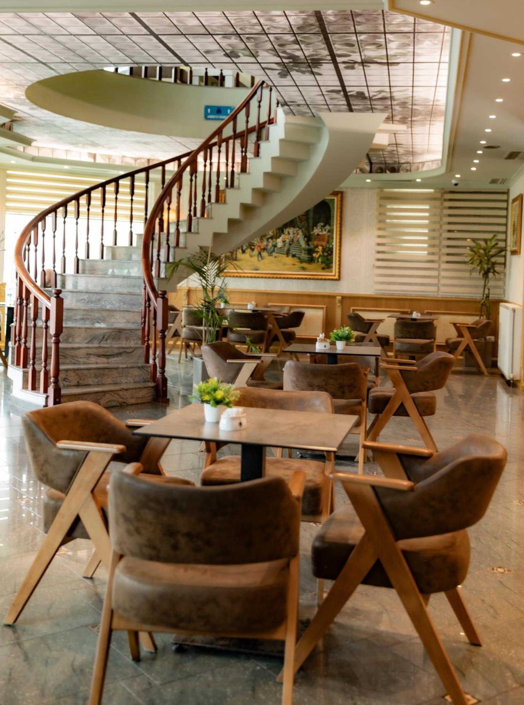 Kafeneja e hollit me shkallë spirale, kolltukë ngjyrë kafe dhe tavolina me bimë të vogla